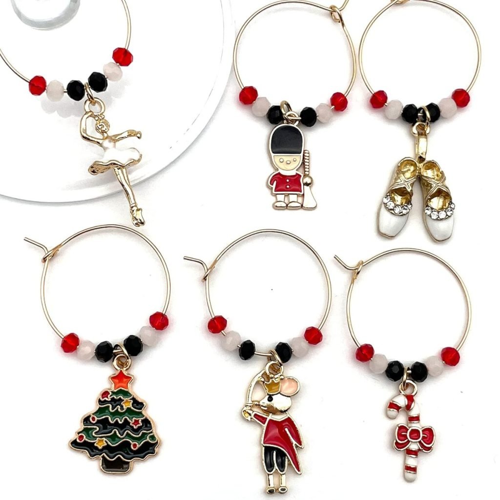 Six wine glass charms featuring various Christmas and ballet-themed designs, including a ballerina, toy soldier, ballet shoes, Christmas tree, mouse, and candy cane.