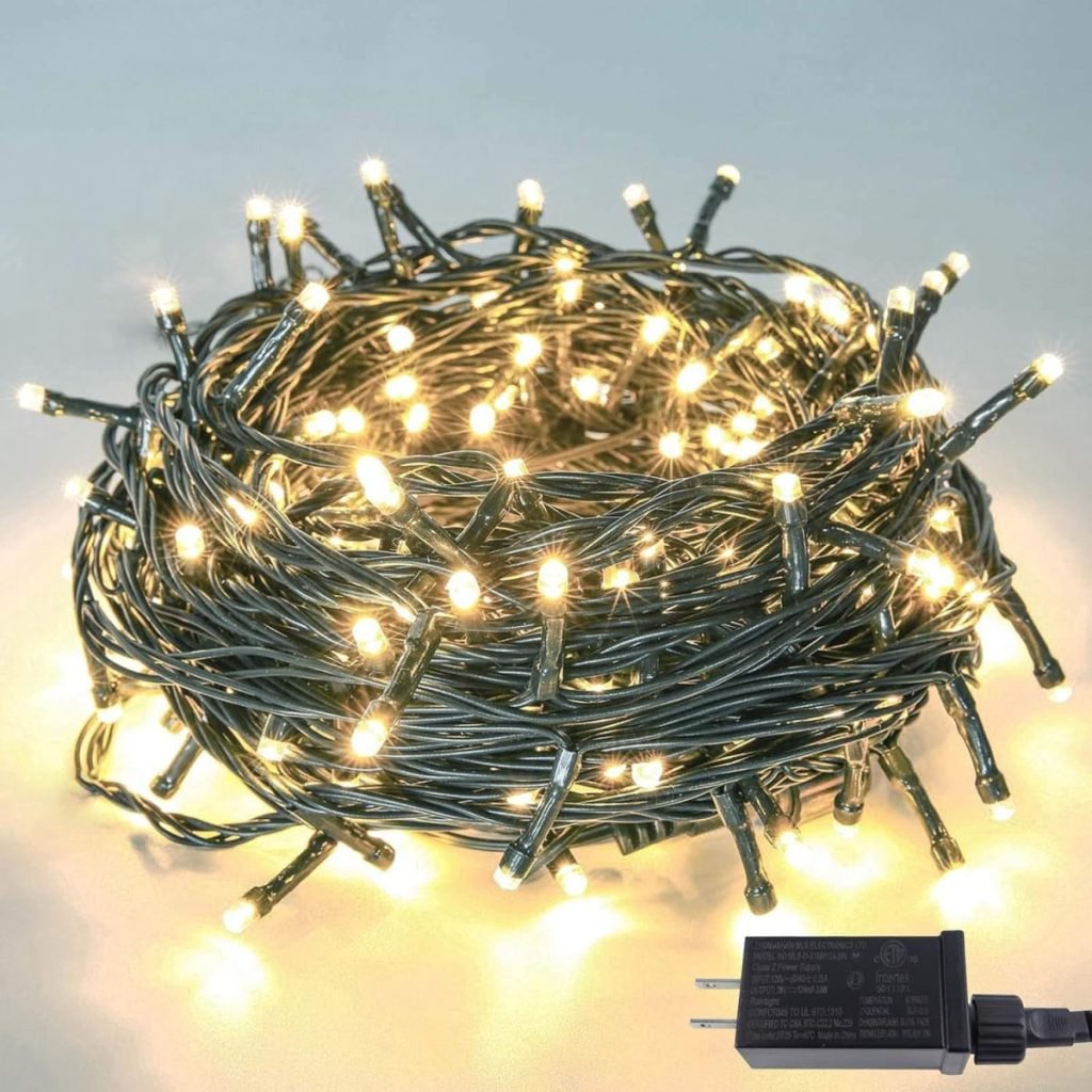 A coiled string of glowing white LED fairy lights with a black plug-in adapter on a light surface.