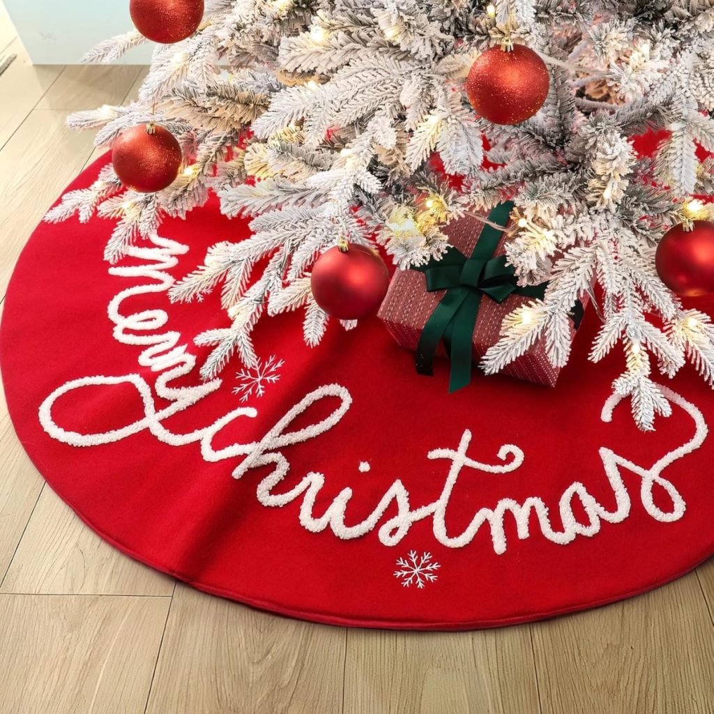 A white Christmas tree adorned with red baubles graces a festive scene, standing proudly on a cheerful Christmas tree skirt that reads "Merry Christmas." Beneath its branches, a gift wrapped in red paper with a green bow awaits discovery.