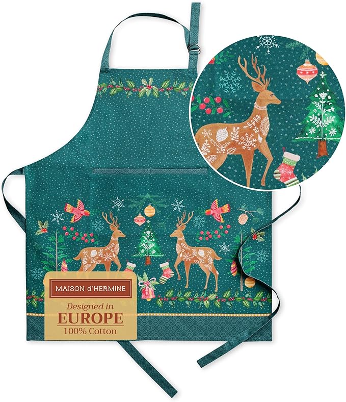 Green cotton apron with a holiday design featuring reindeer, birds, ornaments, snowflakes, and festive Christmas tree cupcakes. Includes a close-up inset of the pattern and a label stating "Designed in Europe.