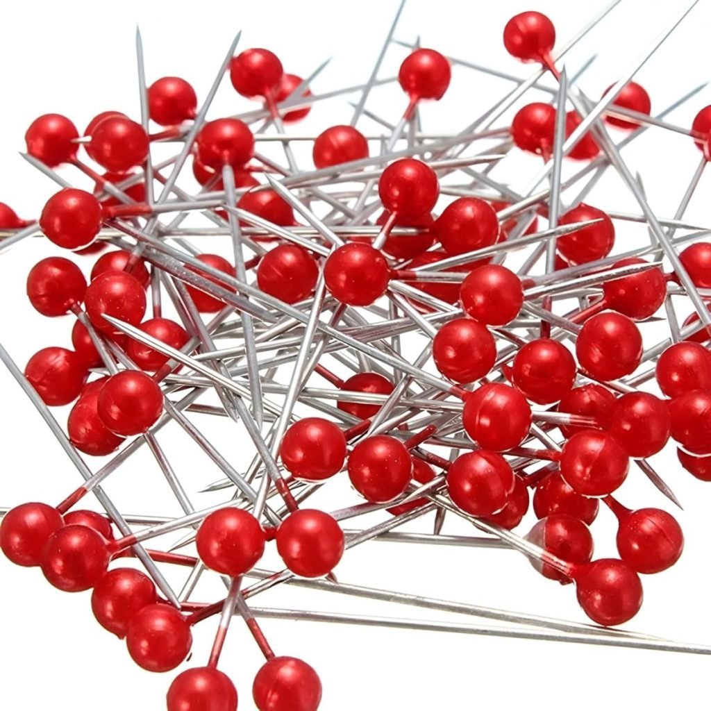 A pile of silver pins with red round heads, perfect for button crafts, scattered on a white surface.