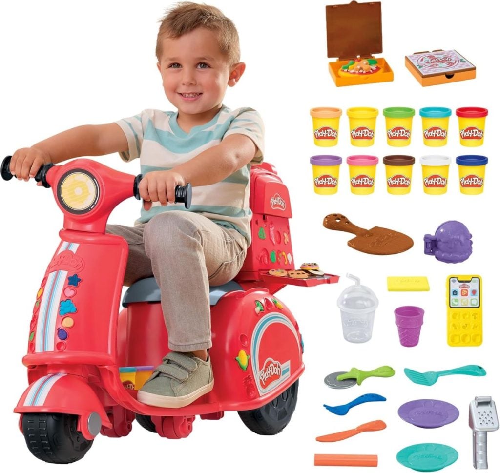 A child on a red toy scooter is surrounded by Play-Doh containers and accessories, including a pretend pizza set, utensils, and molds, creating a scene as whimsical as a Nutcracker Christmas.