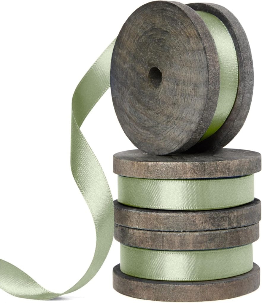 Four rolls of green ribbon on wooden spools, with one ribbon partially unrolled—perfect for your next button crafts project.