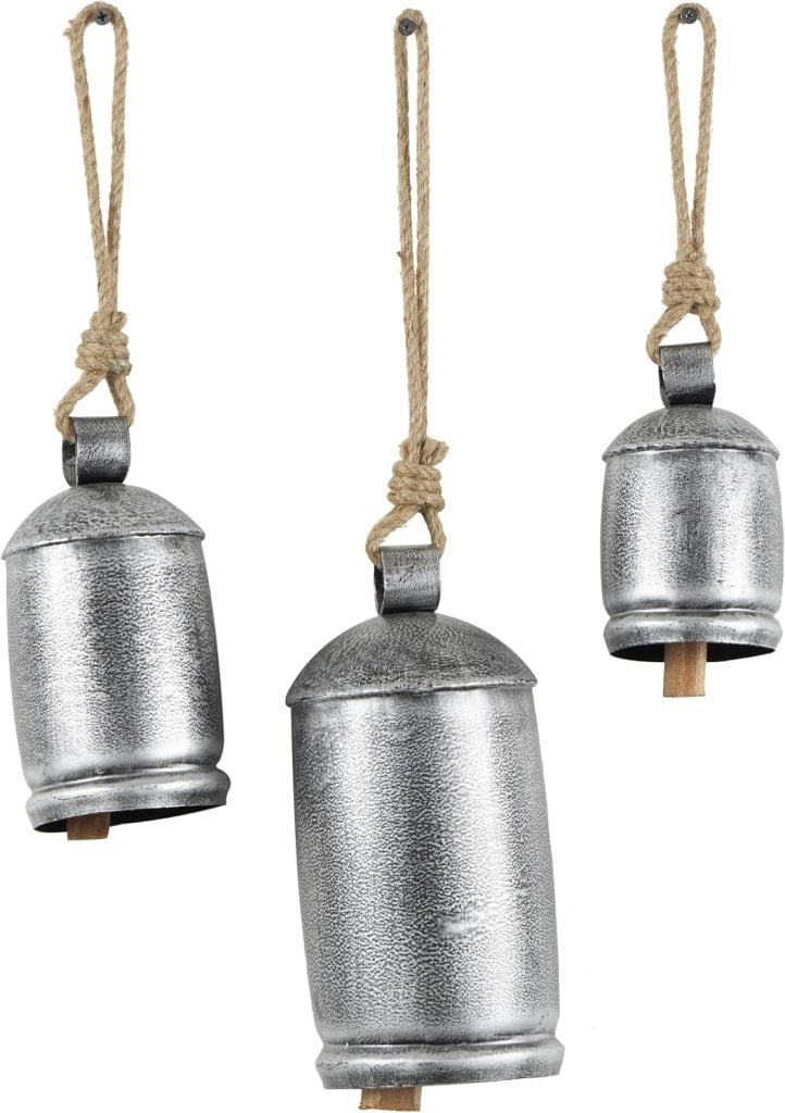 Three metal bells of varying sizes, adorned in Christmas colors, hang from ropes against a white background.