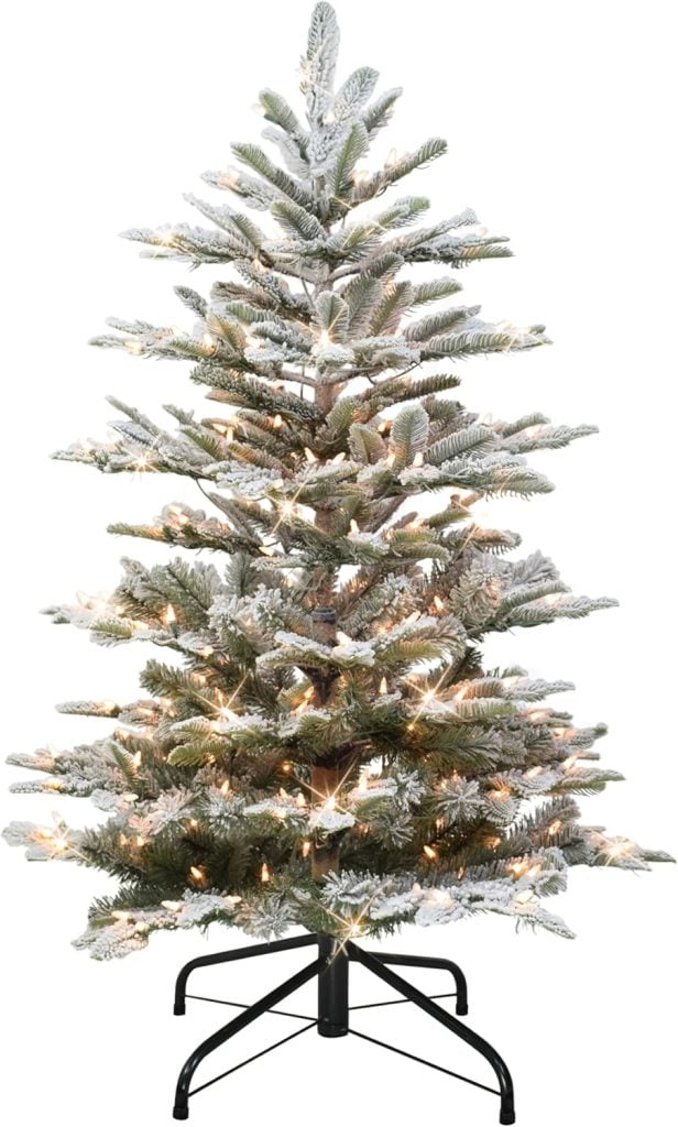 Artificial Christmas tree with snow-covered branches and white lights, set on a black metal stand.