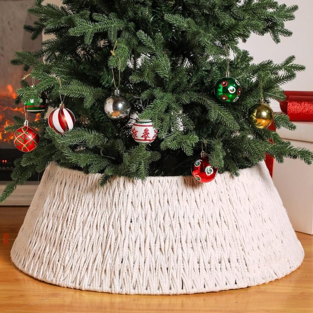 A Christmas tree adorned with decorative ornaments stands in a woven white tree collar, which elegantly covers the traditional Christmas tree skirt on the wooden floor.