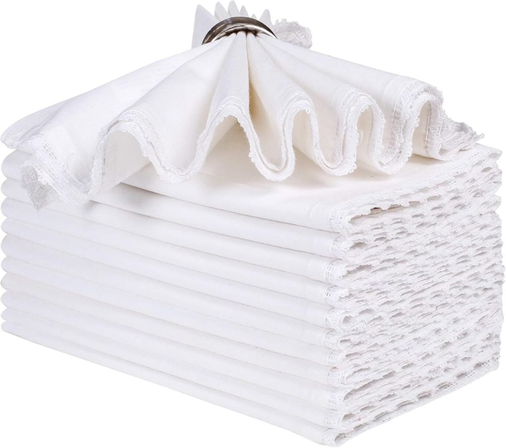 A stack of white linen napkins with lace edges, topped with a napkin ring arranged in a fan shape.