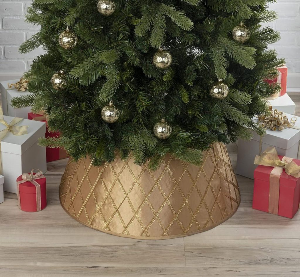 A Christmas tree with golden ornaments and a luxurious, quilted gold christmas tree skirt, surrounded by wrapped gifts in white and red boxes.