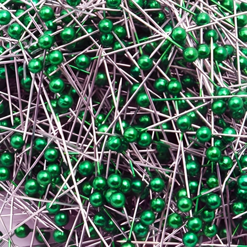 A tangled heap of sewing pins with shiny green round heads and metal shafts lay intertwined haphazardly, perfect for those creative button crafts.