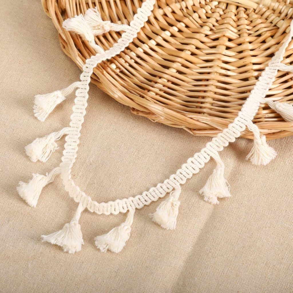 A woven basket and a beige fabric adorned with a cream-colored tassel trim, perfect for displaying your latest crafting skills, such as how to tie a bow.