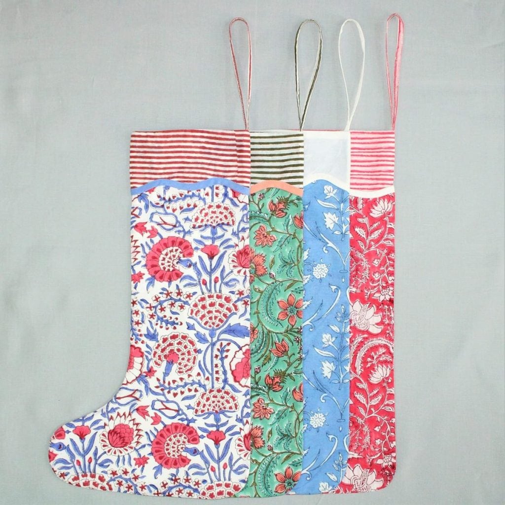 A Christmas stocking made from four vertical panels of patterned fabric in red, green, blue, and white, with striped trim and four hanging loops at the top—perfect for brightening up your Christmas Morning.