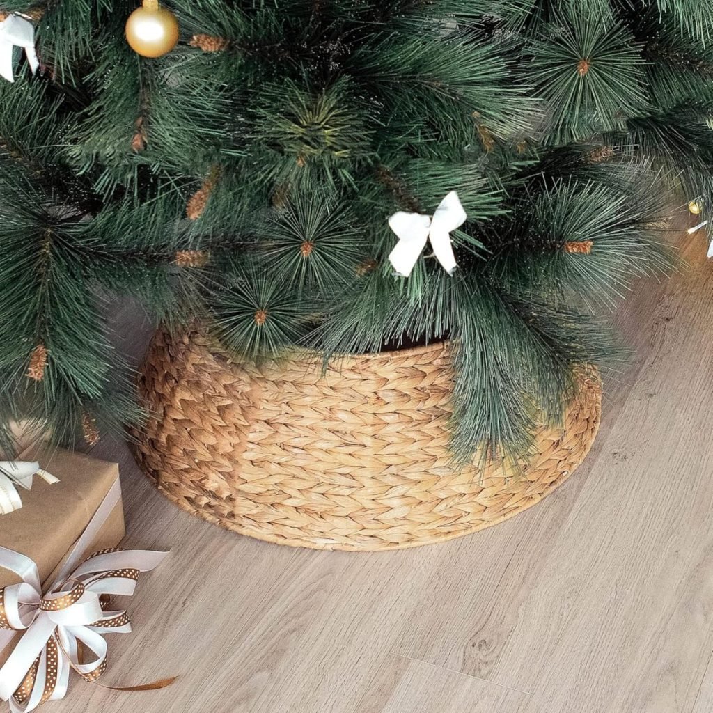 Close-up of a Christmas tree base in a woven basket cover, adorned with gifts wrapped in brown paper and ribbon, reflecting classic Christmas colors on the wooden floor.