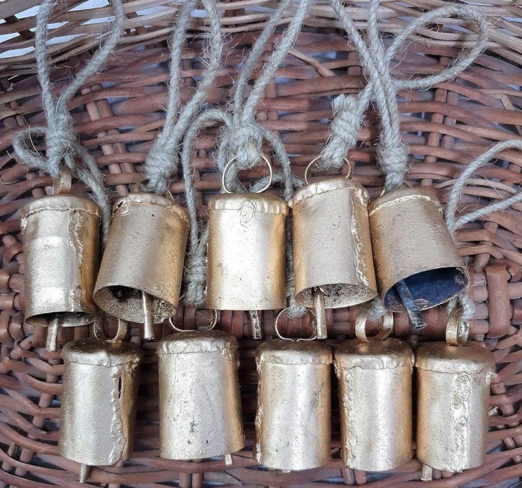 Ten metallic bells with braided rope handles are arranged on a woven basket surface, each accented with a festive Christmas ribbon.