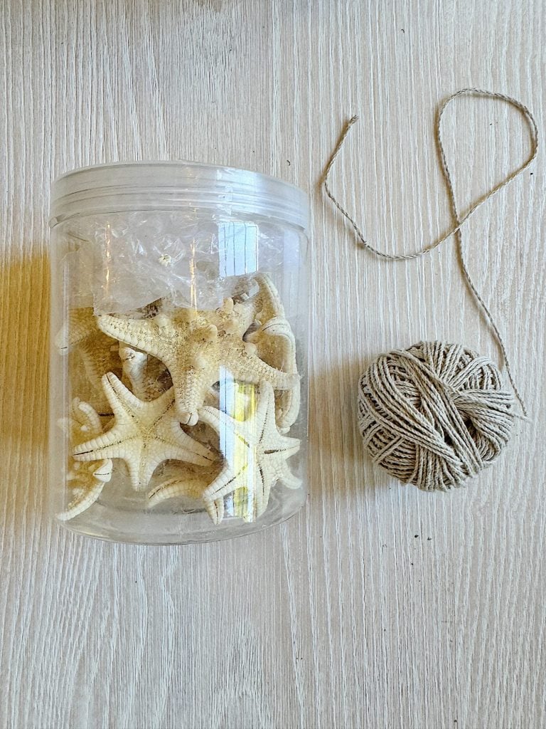 A clear plastic jar with starfish beside a ball of twine on a light wooden surface.