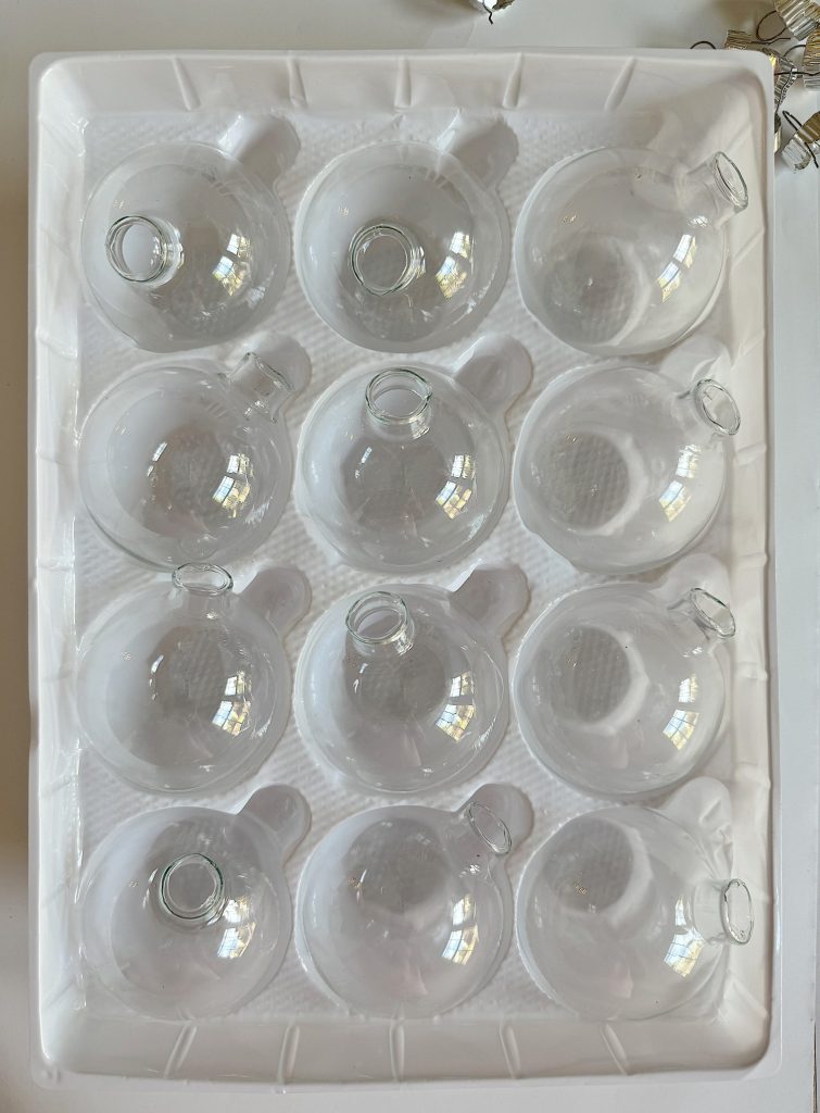 A tray containing twelve clear glass ornaments, arranged in a 3x4 grid.