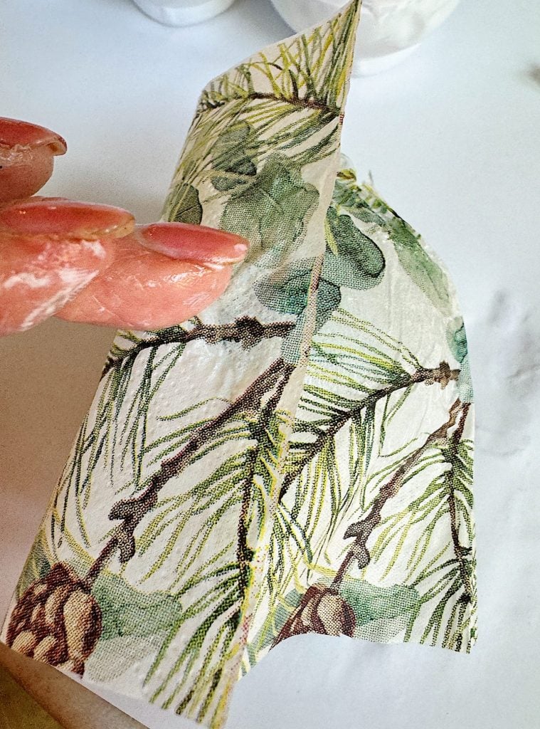 Person holding a decorative napkin with a pine branch and cone pattern.