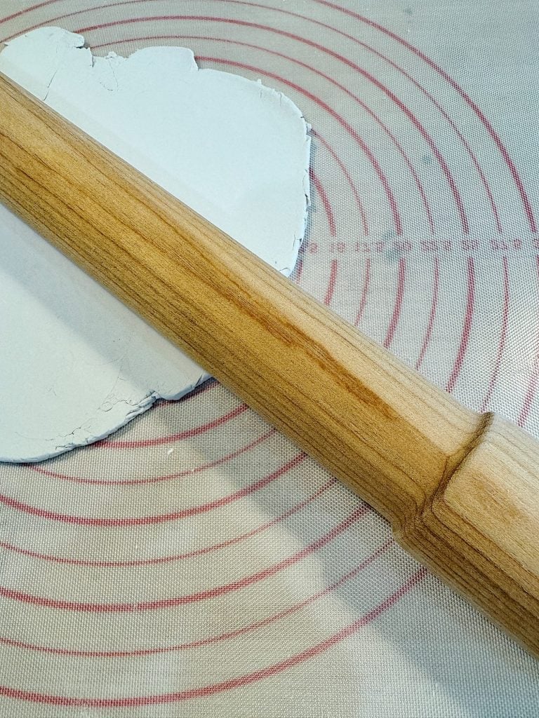 A wooden rolling pin on a dough mat, flattening white dough.