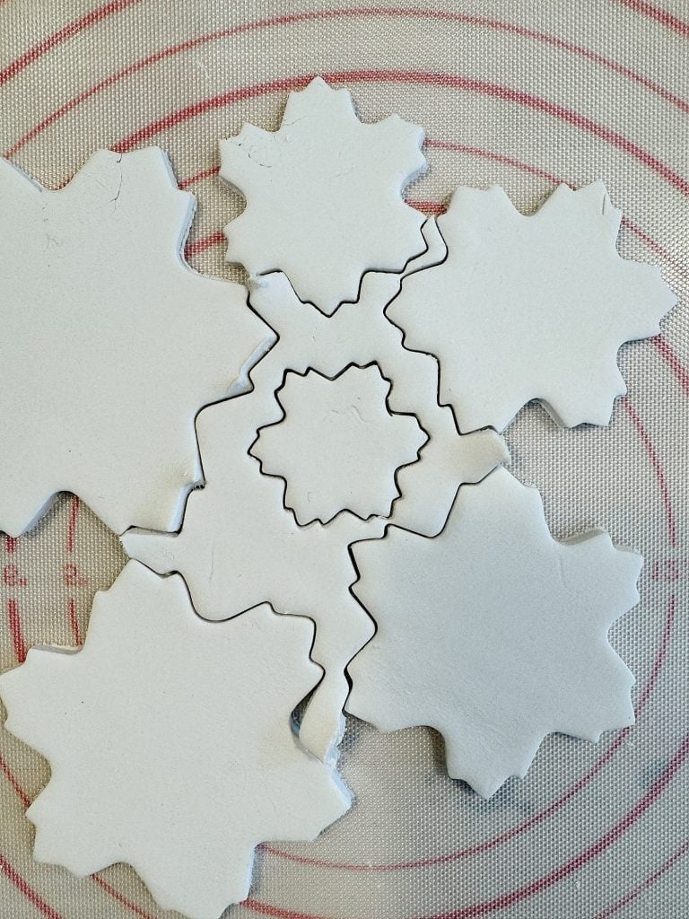 Six white snowflake-shaped clay pieces arranged on a circular grid mat.