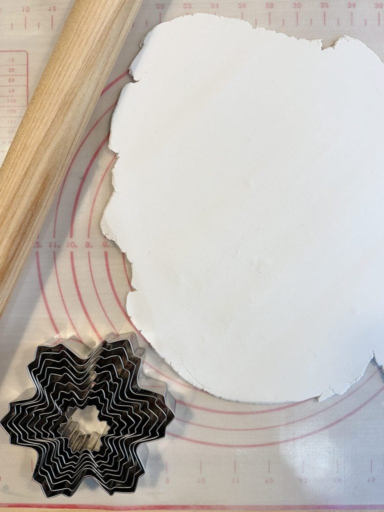 Wooden rolling pin with white dough on a red-lined mat next to a stack of star-shaped cookie cutters.