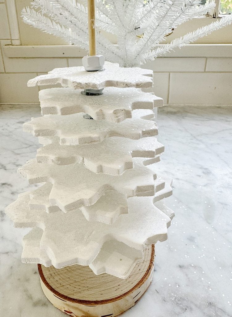 Stacked white foam snowflakes arranged to resemble a Christmas tree, on a wooden base, placed on a marble countertop.