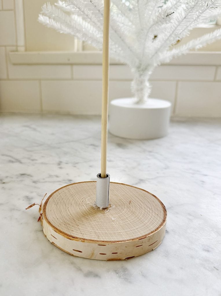 Wooden base with a vertical dowel, standing on a marble surface, with a white decorative object in the background.