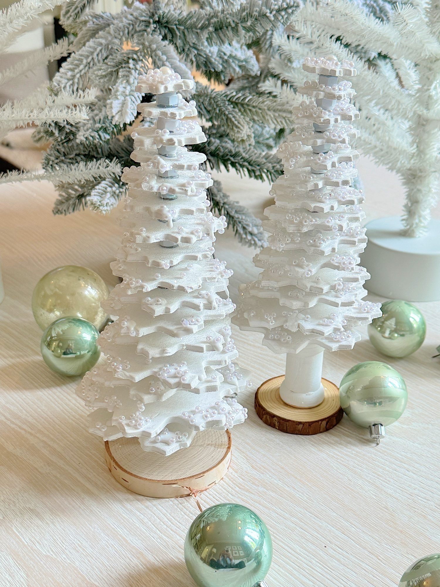 Two decorative white tabletop Christmas trees with beaded details, surrounded by light green ornaments.