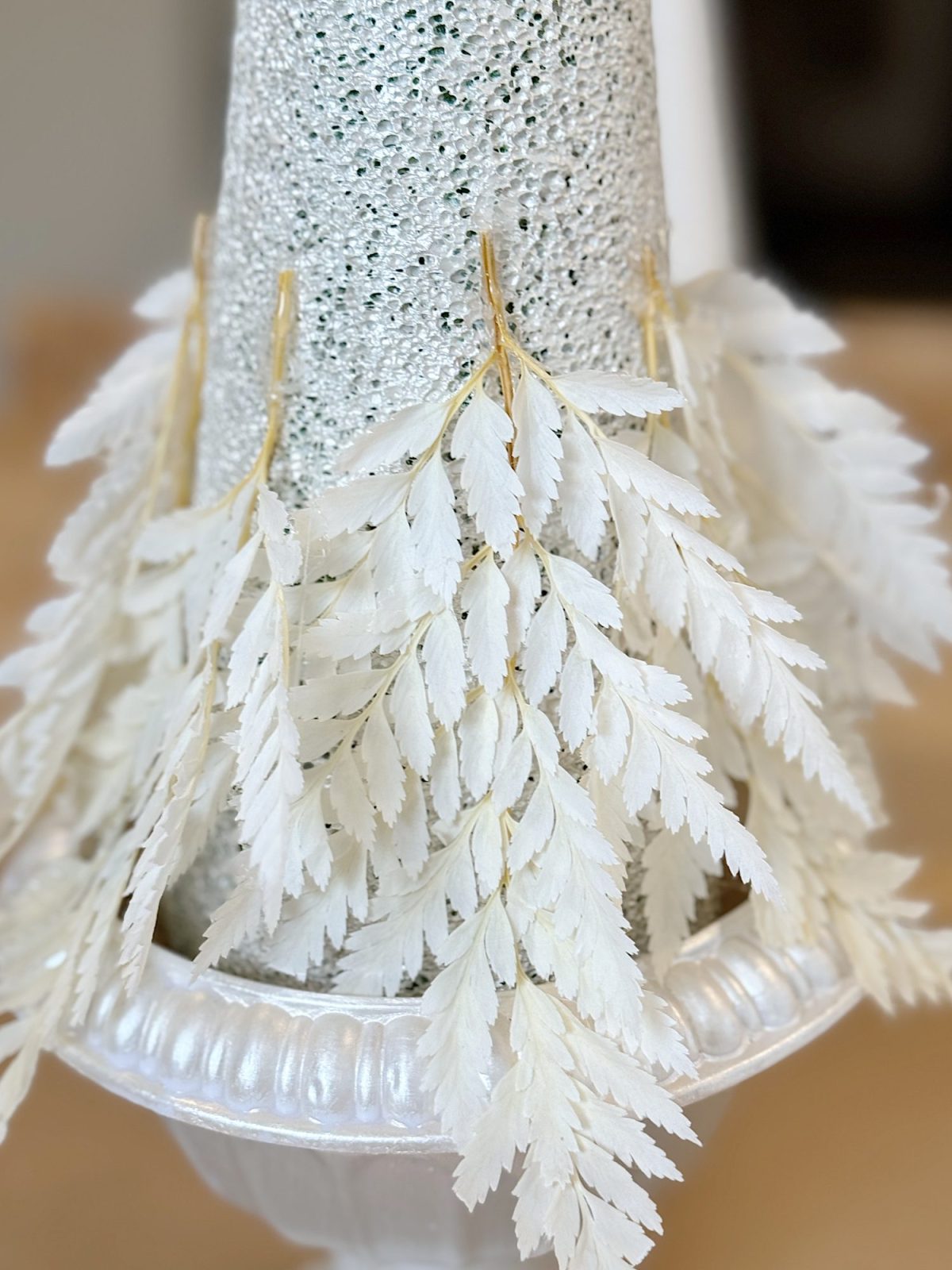 Sparkly silver cone adorned with cascading white leaves in a decorative pot.