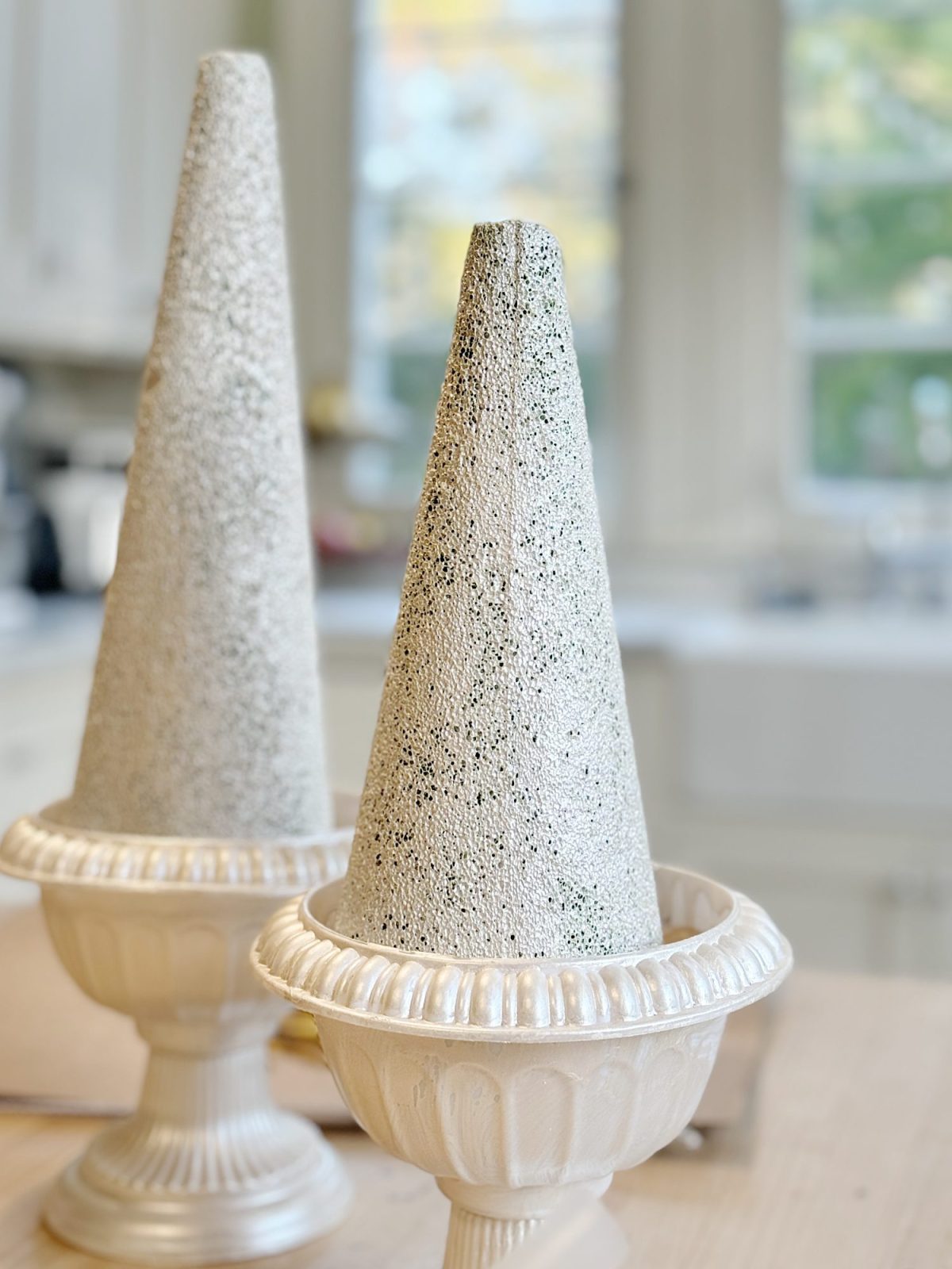 Two textured cone-shaped sculptures sit in ornate white bases on a kitchen counter.