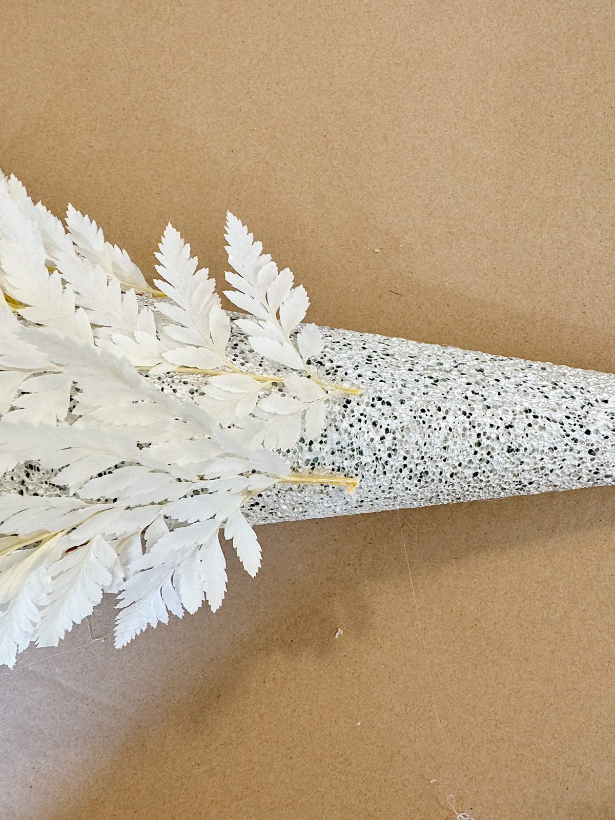 A speckled gray cone holds dry, white fern leaves on a plain brown surface.