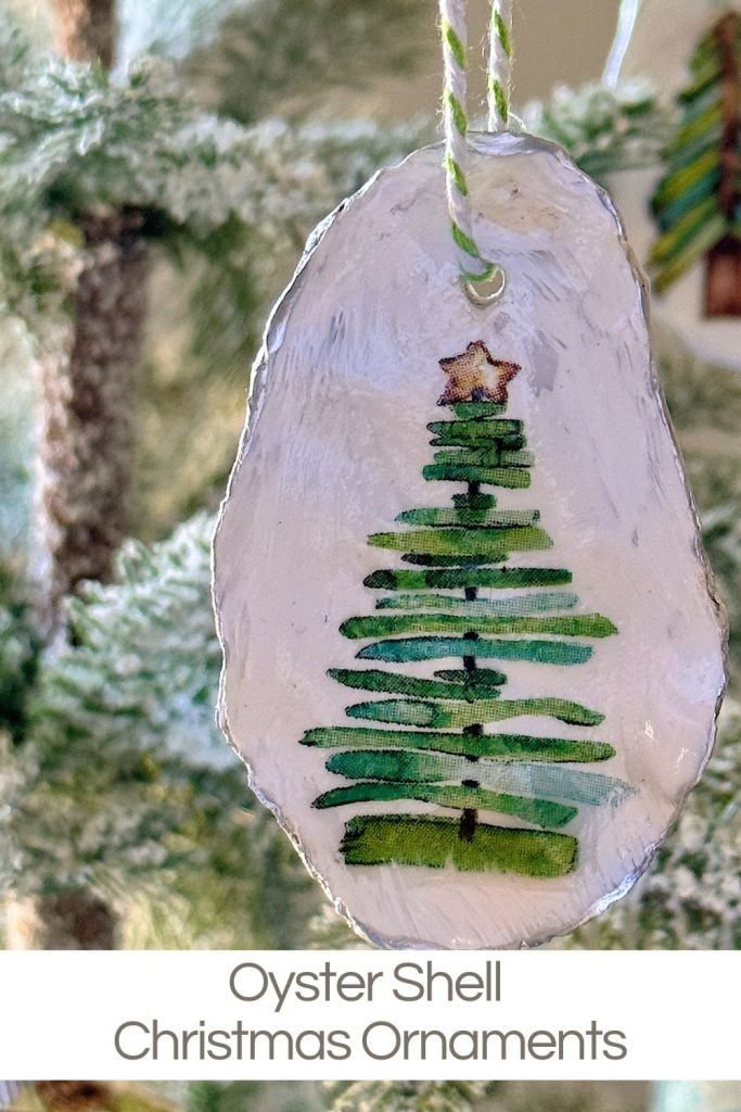 An oyster shell ornament painted with a green Christmas tree and star, hanging on a string.