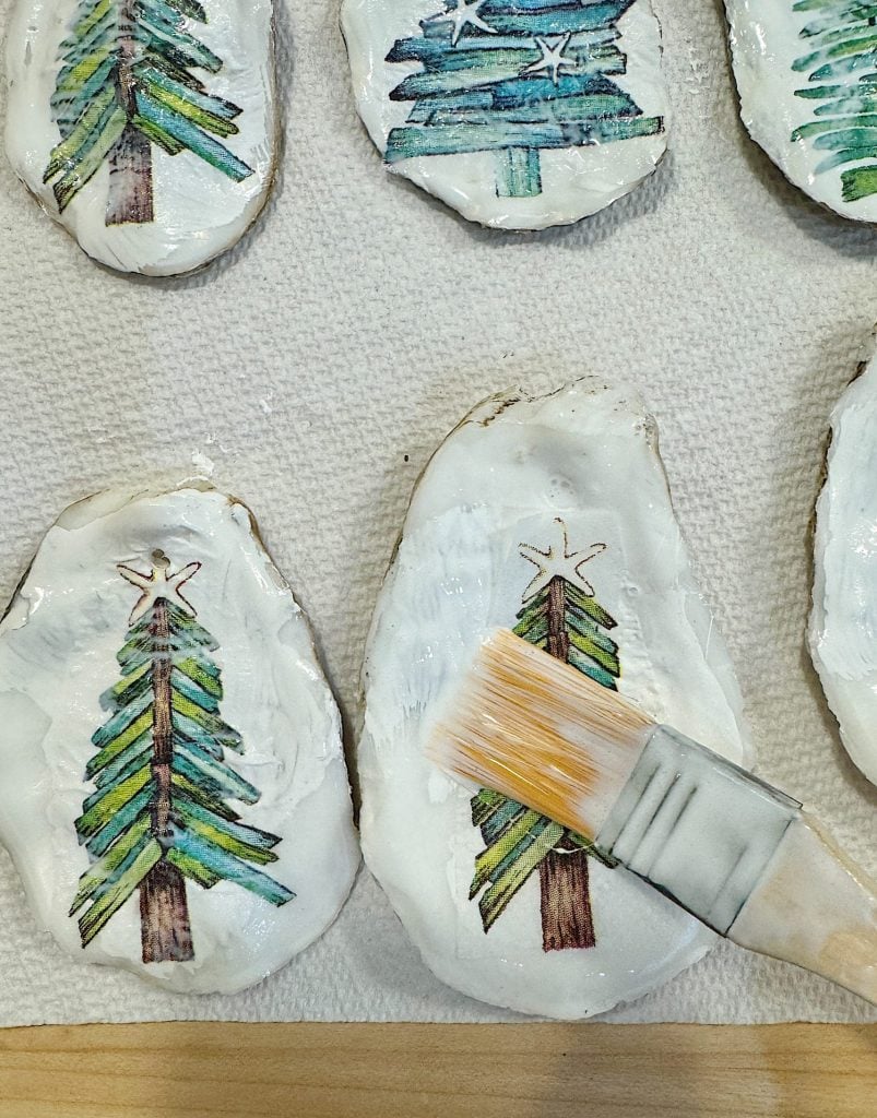 Painted tree designs on rocks are being coated with a clear substance using a brush.