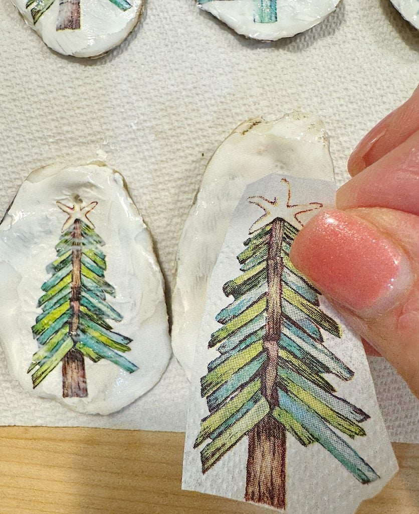 Person applying a paper transfer of a Christmas tree design onto a white clay surface with a star shape at the top.