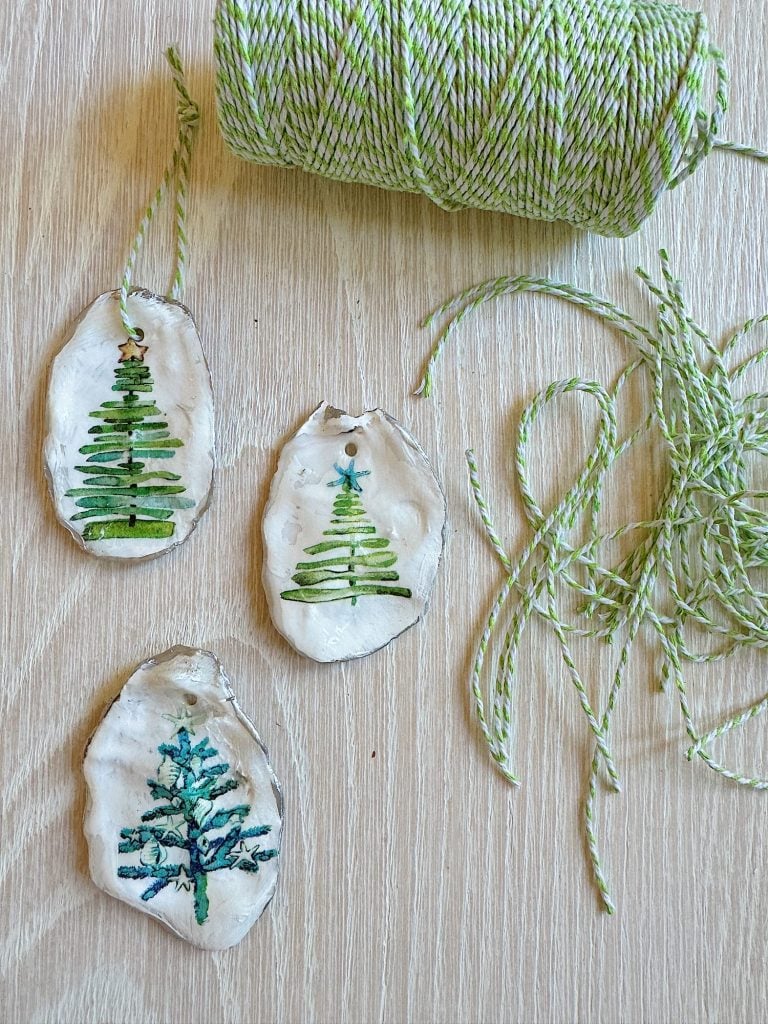 Clay ornaments with green tree designs are placed on a wooden surface next to a spool of green and white twine.