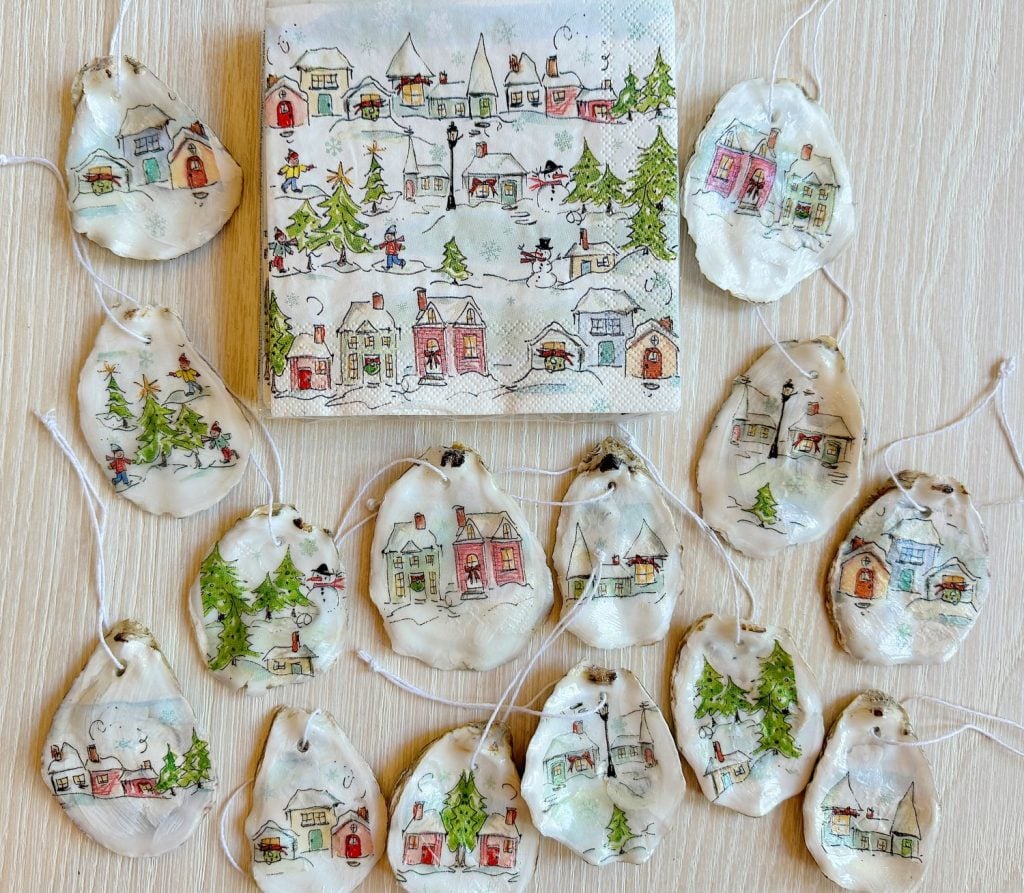 Handcrafted ornaments and a matching napkin featuring illustrations of winter village scenes with houses, trees, and people.