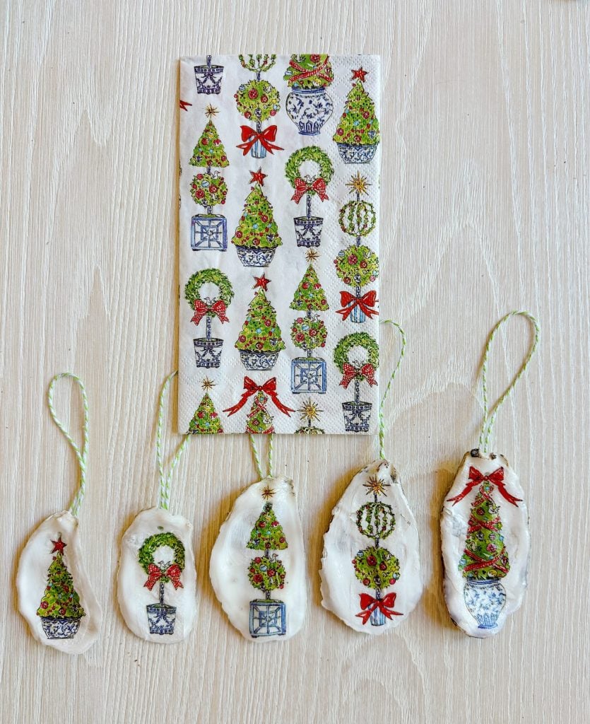 Five small decorations with Christmas tree designs in front of a matching napkin on a wooden surface.