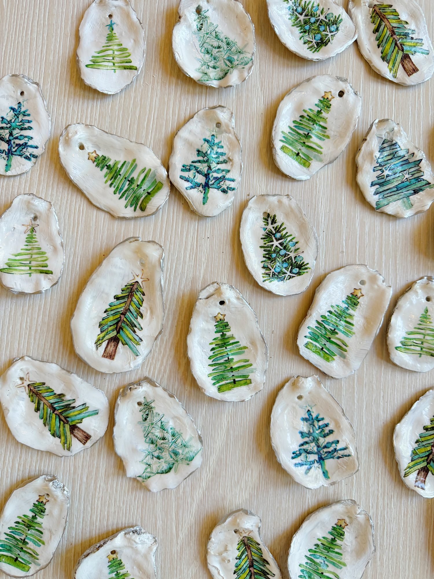 Oyster shells painted with green Christmas tree designs are arranged on a wooden surface.