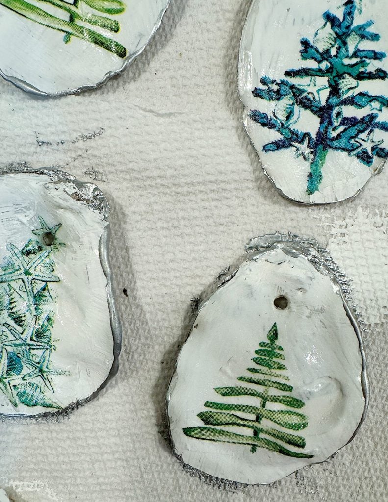 Four painted stone ornaments with various green and blue tree designs are placed on a textured white surface.