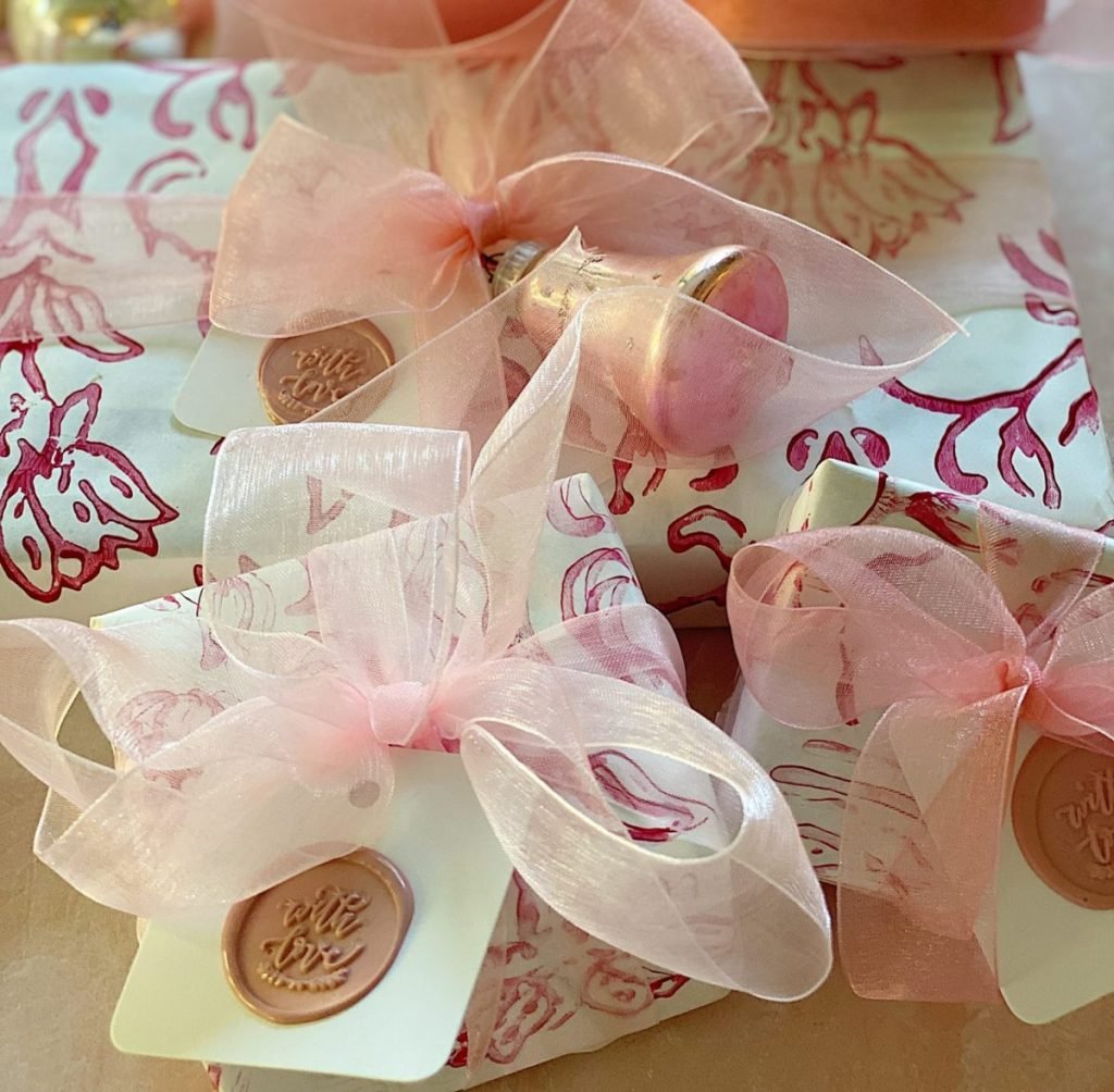 Gift boxes featuring exquisite gift wrapping in floral paper, tied with pink ribbons and sealed with wax stamps adorned with "with love" inscriptions.