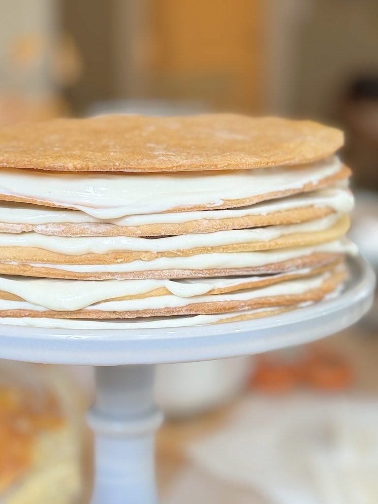 A multi-layered cake with thin layers of pastry and white cream filling on a blue cake stand.