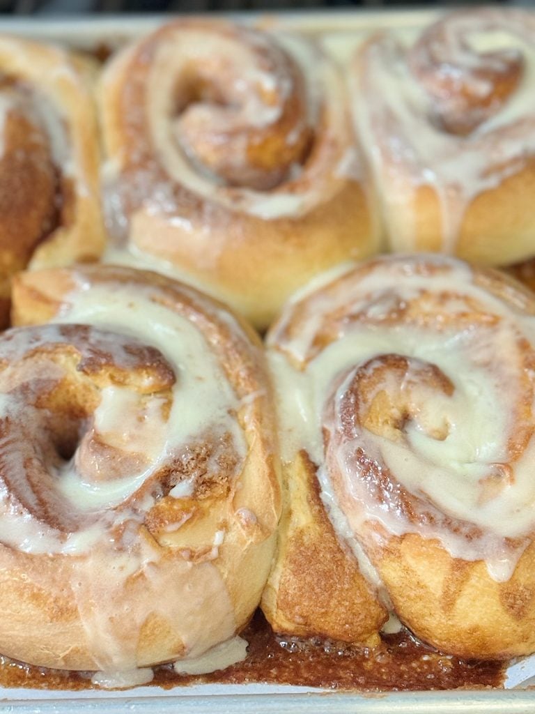 Close-up of freshly baked cinnamon rolls with icing on top, arranged in a baking tray.