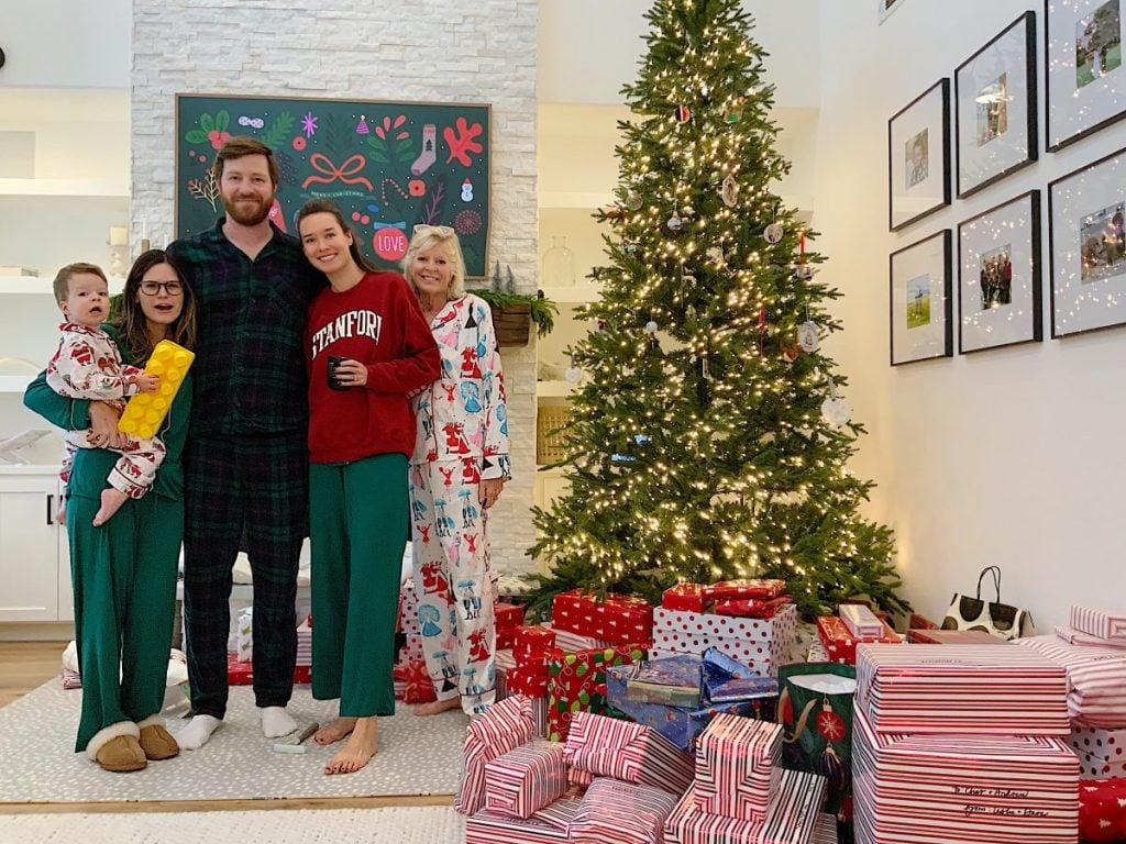 Five people in pajamas stand in front of a decorated Christmas tree and a pile of wrapped presents in a living room, capturing the joy of Christmas Morning as they pose for a festive holiday photo.