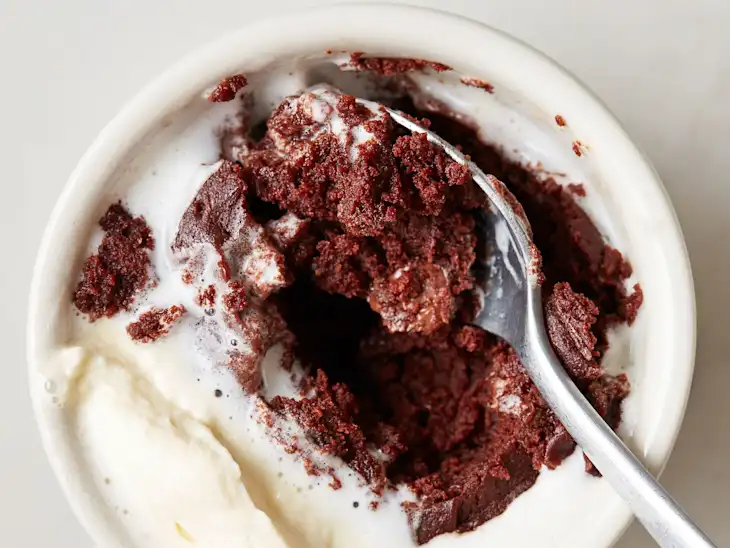 A bowl of chocolate cake with a spoon on the side, partially topped with whipped cream.