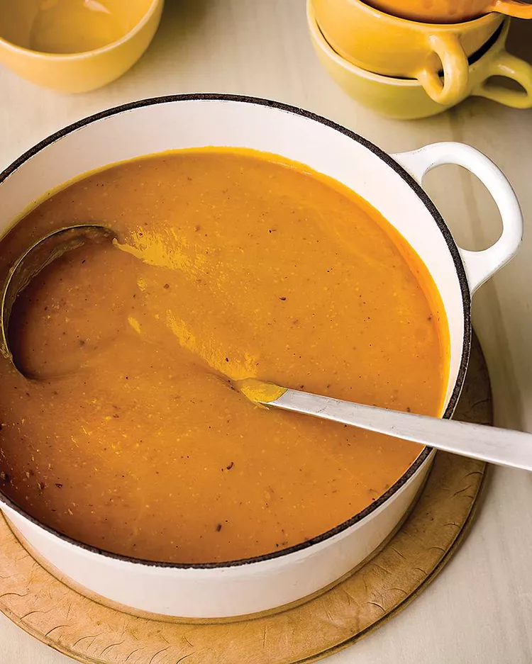 A pot of creamy orange soup with a ladle, perfectly placed on a wooden board, brings warmth to any Black Friday feast.