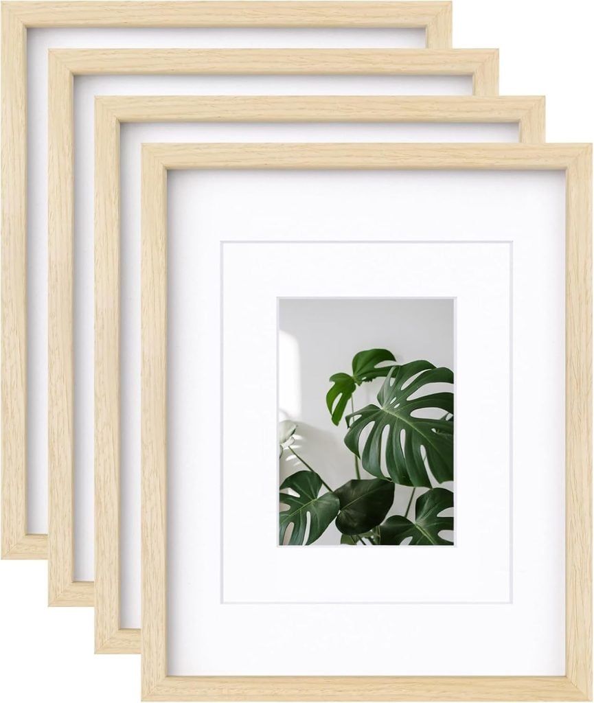 Four wooden picture frames in a stack, one displaying a monstera leaf image.