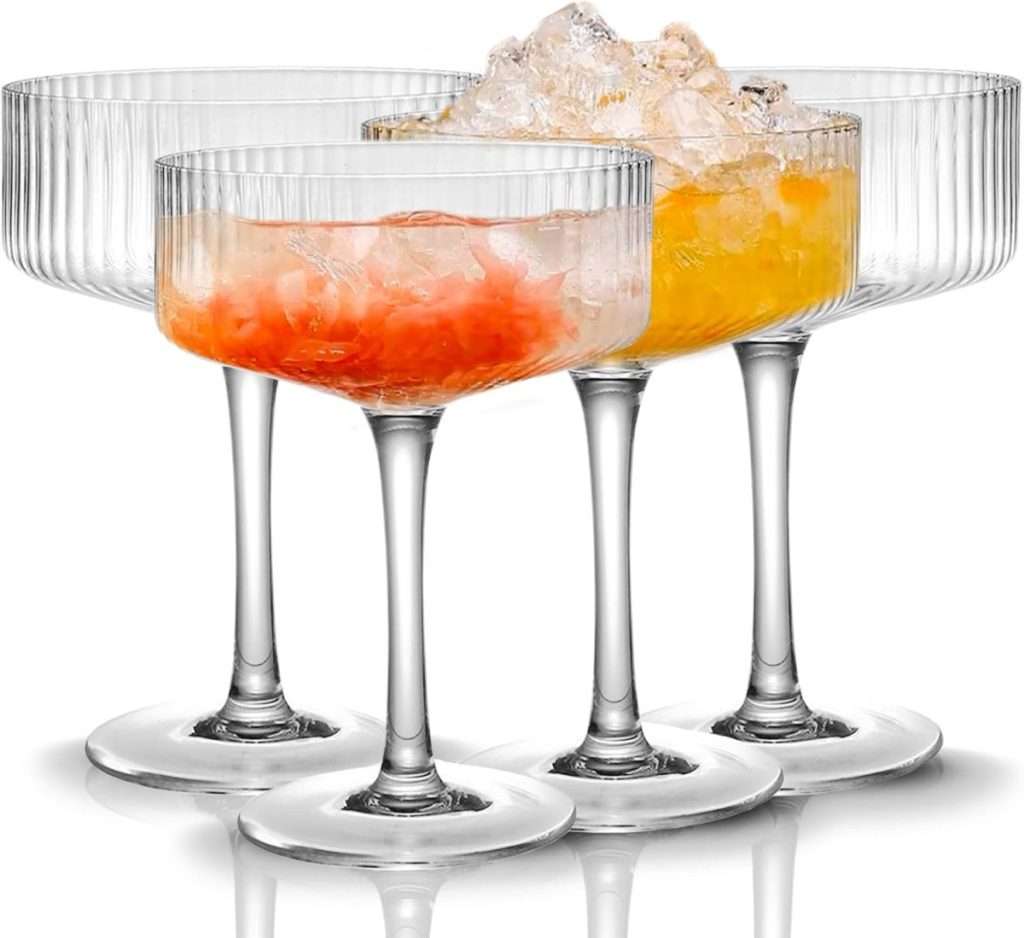 Four ribbed coupe glasses, two filled with orange cocktails and crushed ice, are arranged in a row on a white background—perfect for toasting during the season of giving.