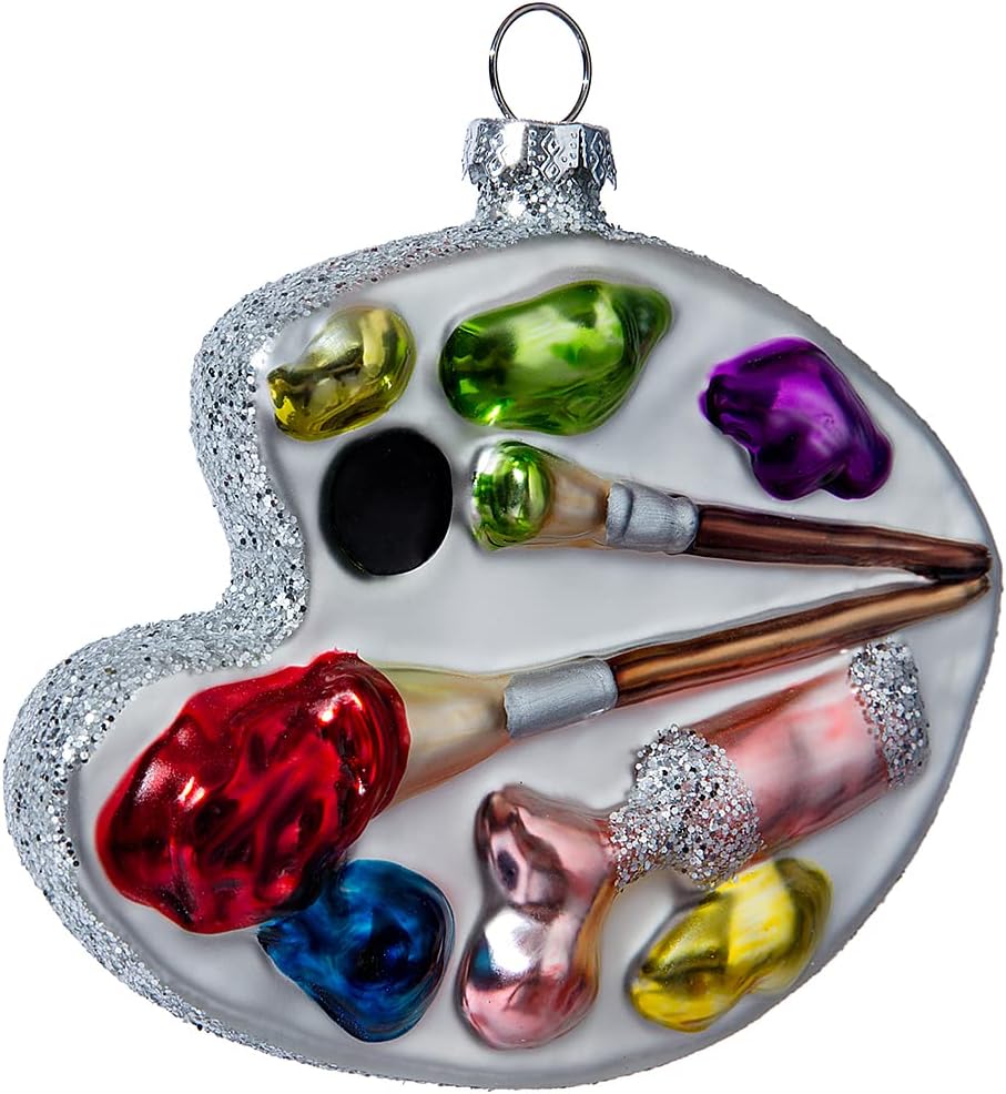 A Christmas ornament exuding Christmas joy, shaped like a painter's palette with colorful paint dabs and two paintbrushes, silver accents, and a metal loop for hanging.