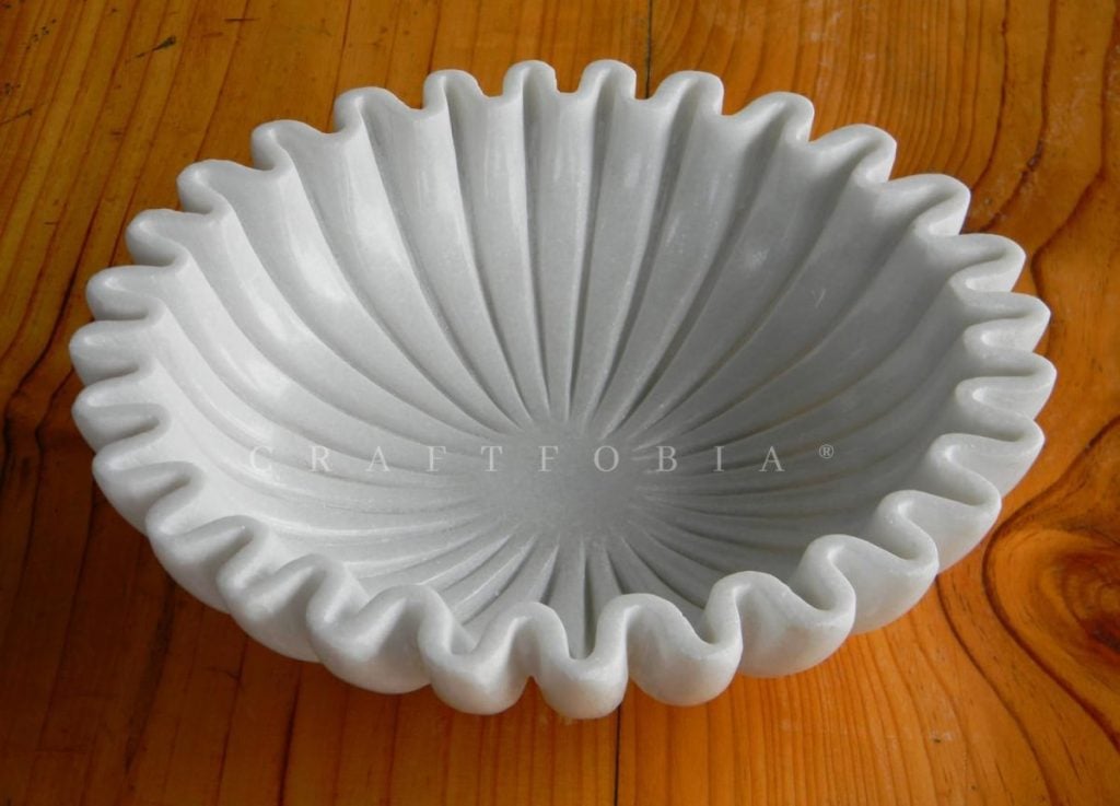 White scalloped ceramic bowl with vertical ribbed pattern, placed on a wooden surface.