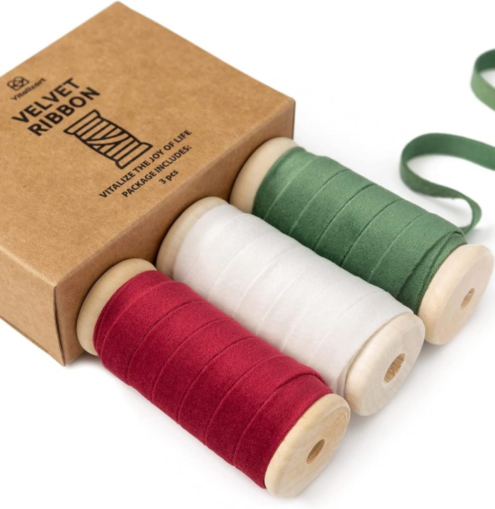 Three spools of ribbon in red, white, and green are displayed beside a brown box labeled "Velvet Ribbon," perfect for adding a touch of Christmas joy to any festive decoration.