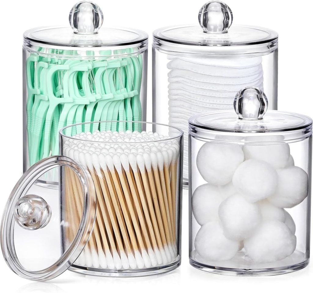 Four transparent canisters containing green flossers, cotton rounds, cotton swabs, and cotton balls. One canister lid is slightly ajar.