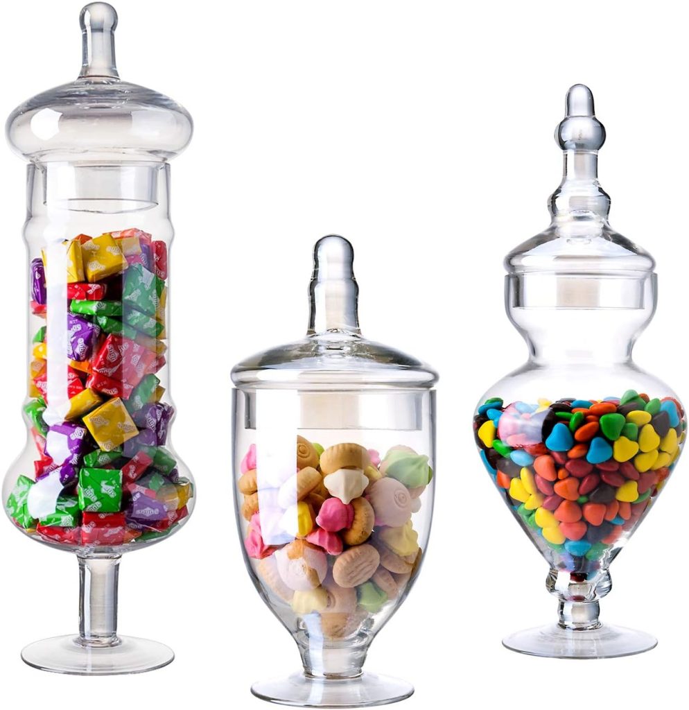 Three clear glass jars with lids, each containing colorful candies—square-shaped chews, pastel candies, and small multicolored pieces—make a cheerful addition to your counter or shelf and can even be used to display Christmas cards creatively.